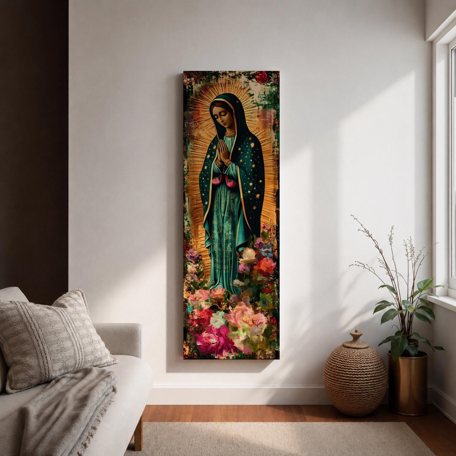 A tall narrow vertical painting of the Virgin Mary Guadalupe shown in prayer with hands clasped, wearing a deep teal mantle adorned with gold stars and a soft pink dress, surrounded by radiant golden rays, with rich floral elements in vibrant pink, red, and cream tones at the base, rendered in a textured painterly style with warm, aged tones.