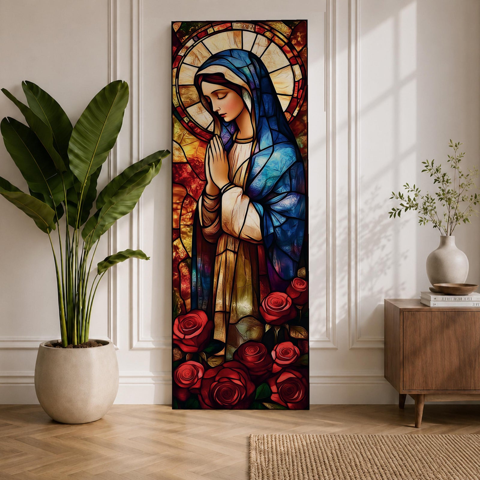 Long vertical stained glass style depiction of the Virgin Mary with hands clasped in prayer. She wears a blue mantle and cream robe while a circular halo glows behind her head and red roses bloom at her feet, all formed with colorful glass segments in a luminous devotional composition.