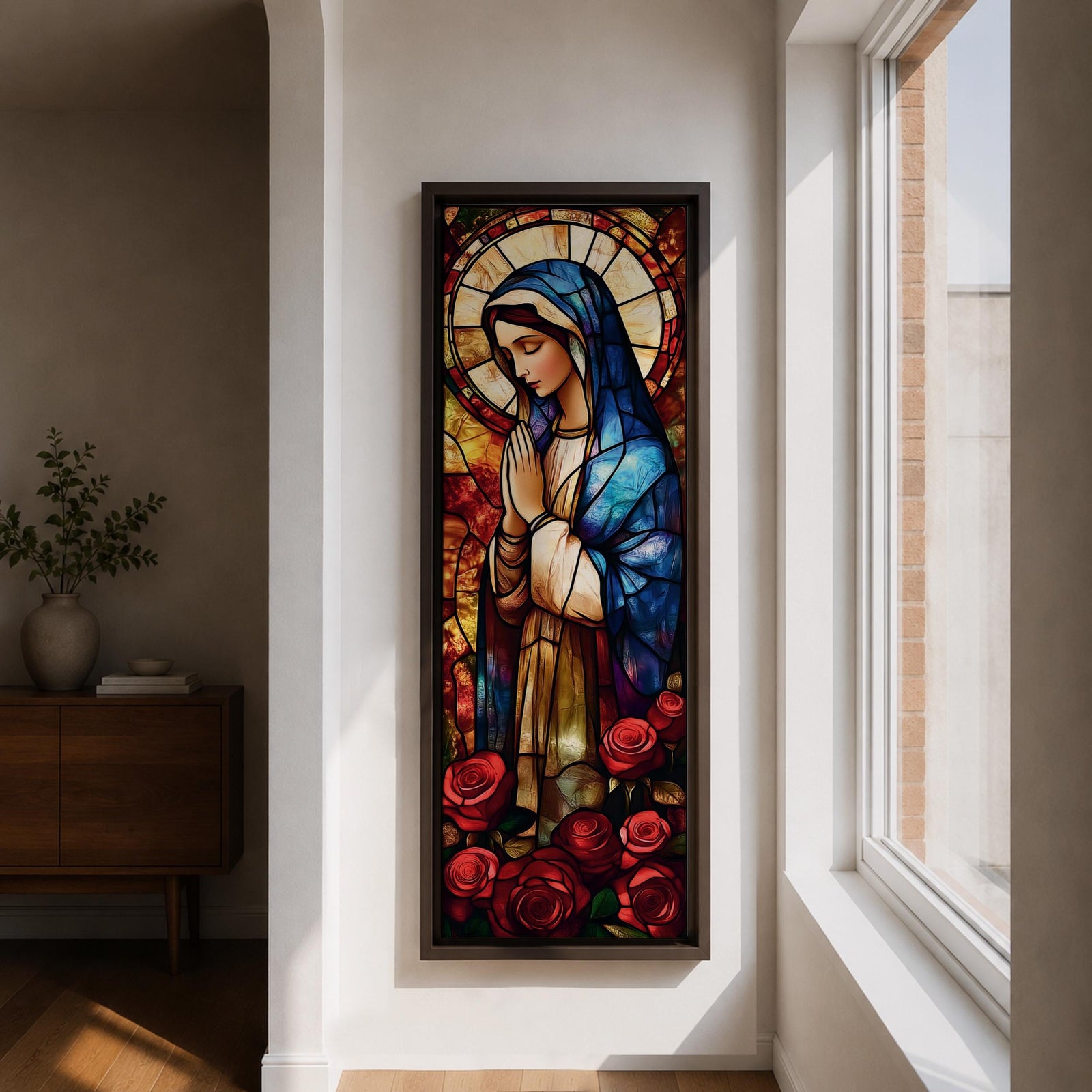 Long vertical stained glass style depiction of the Virgin Mary with hands clasped in prayer. She wears a blue mantle and cream robe while a circular halo glows behind her head and red roses bloom at her feet, all formed with colorful glass segments in a luminous devotional composition.