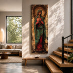 Long vertical painting of the Virgin Mary standing with hands clasped in prayer, wearing a deep red robe and teal mantle. An ornate circular golden halo with sacred symbols forms a radiant backdrop while textured brushwork and aged tones create a traditional Catholic devotional icon style composition.