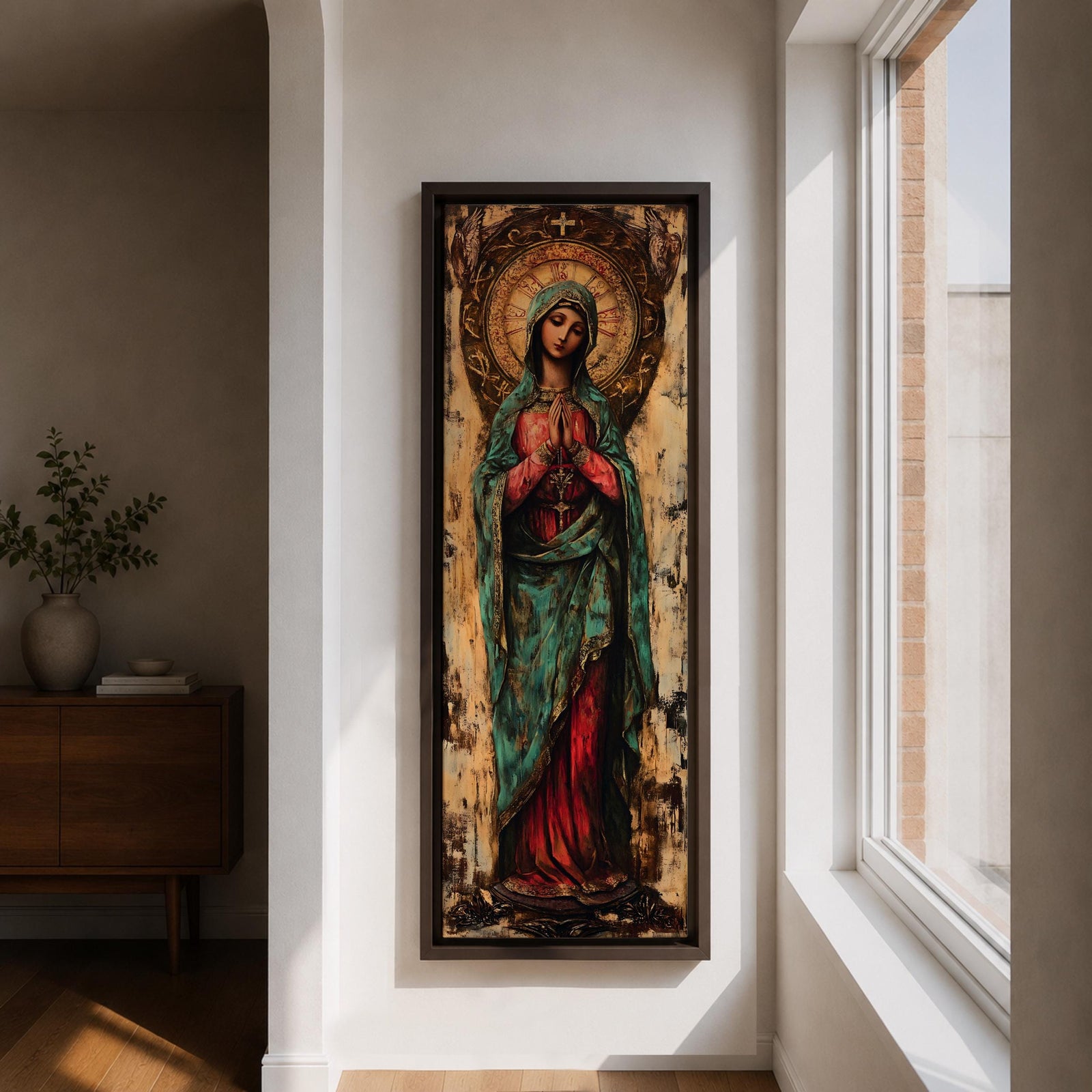Long vertical painting of the Virgin Mary standing with hands clasped in prayer, wearing a deep red robe and teal mantle. An ornate circular golden halo with sacred symbols forms a radiant backdrop while textured brushwork and aged tones create a traditional Catholic devotional icon style composition.