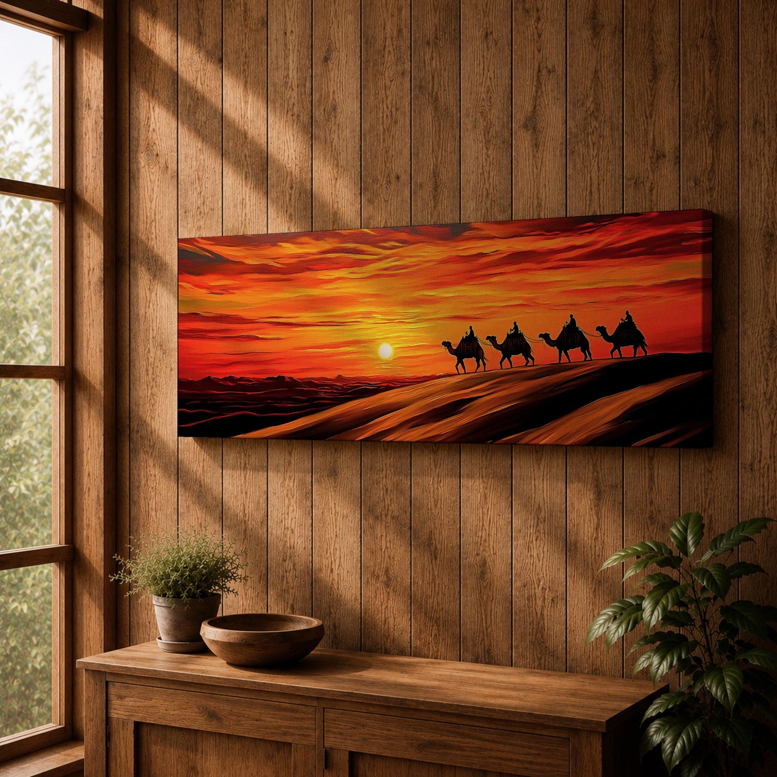 Panoramic desert sunset painting featuring a silhouette caravan of camels and riders walking along rolling sand dunes beneath a glowing red and orange sky. The low sun sits near the horizon while layered desert dunes stretch into the distance, creating a dramatic wide composition across the desert landscape.