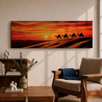 Panoramic desert sunset painting featuring a silhouette caravan of camels and riders walking along rolling sand dunes beneath a glowing red and orange sky. The low sun sits near the horizon while layered desert dunes stretch into the distance, creating a dramatic wide composition across the desert landscape.