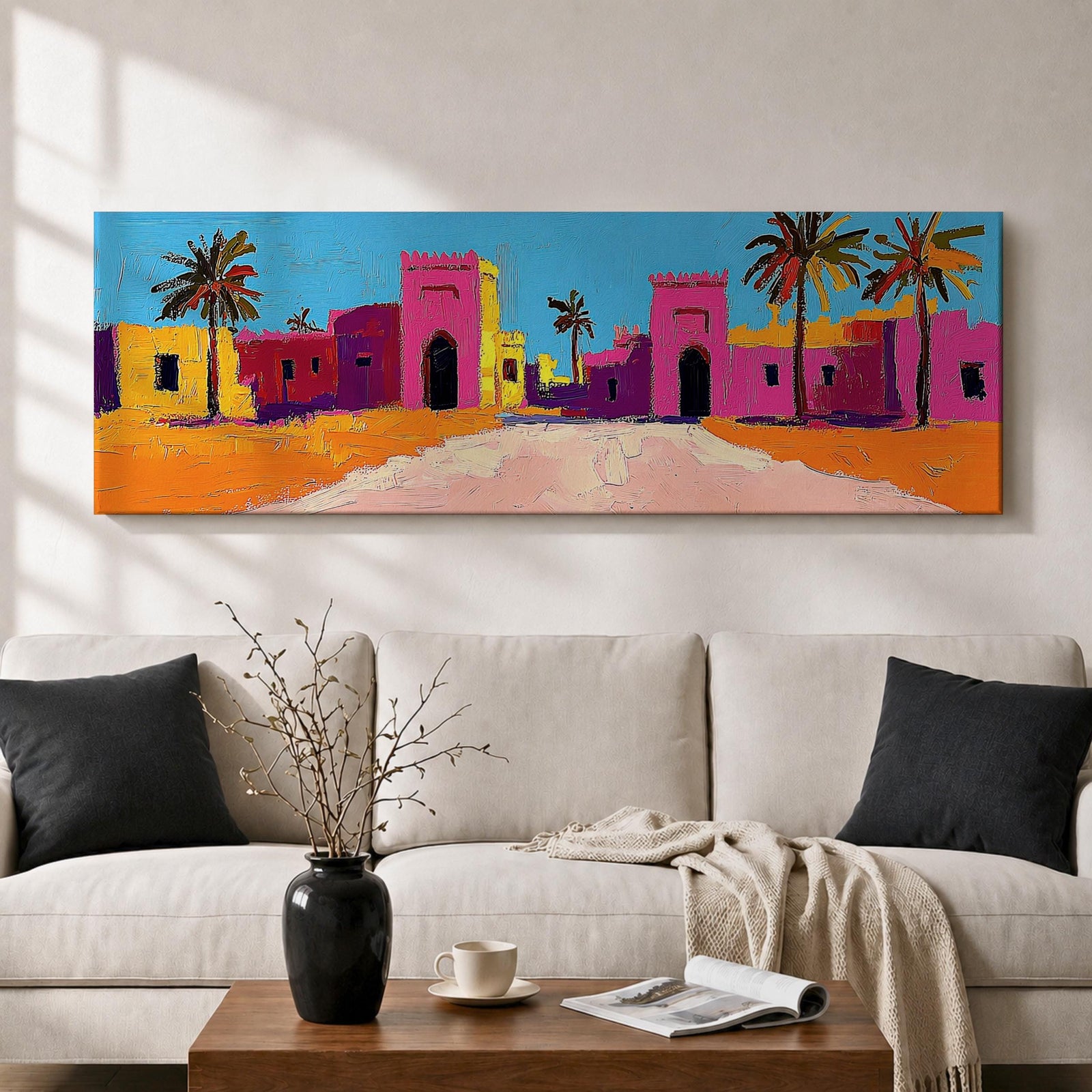 Panoramic desert village painting showing colorful Moroccan kasbah buildings in bright pink and warm ochre tones with tall palm trees lining a sandy road. Bold textured brushstrokes and vibrant colors create a lively North African scene beneath a clear blue sky across the wide horizontal composition.
