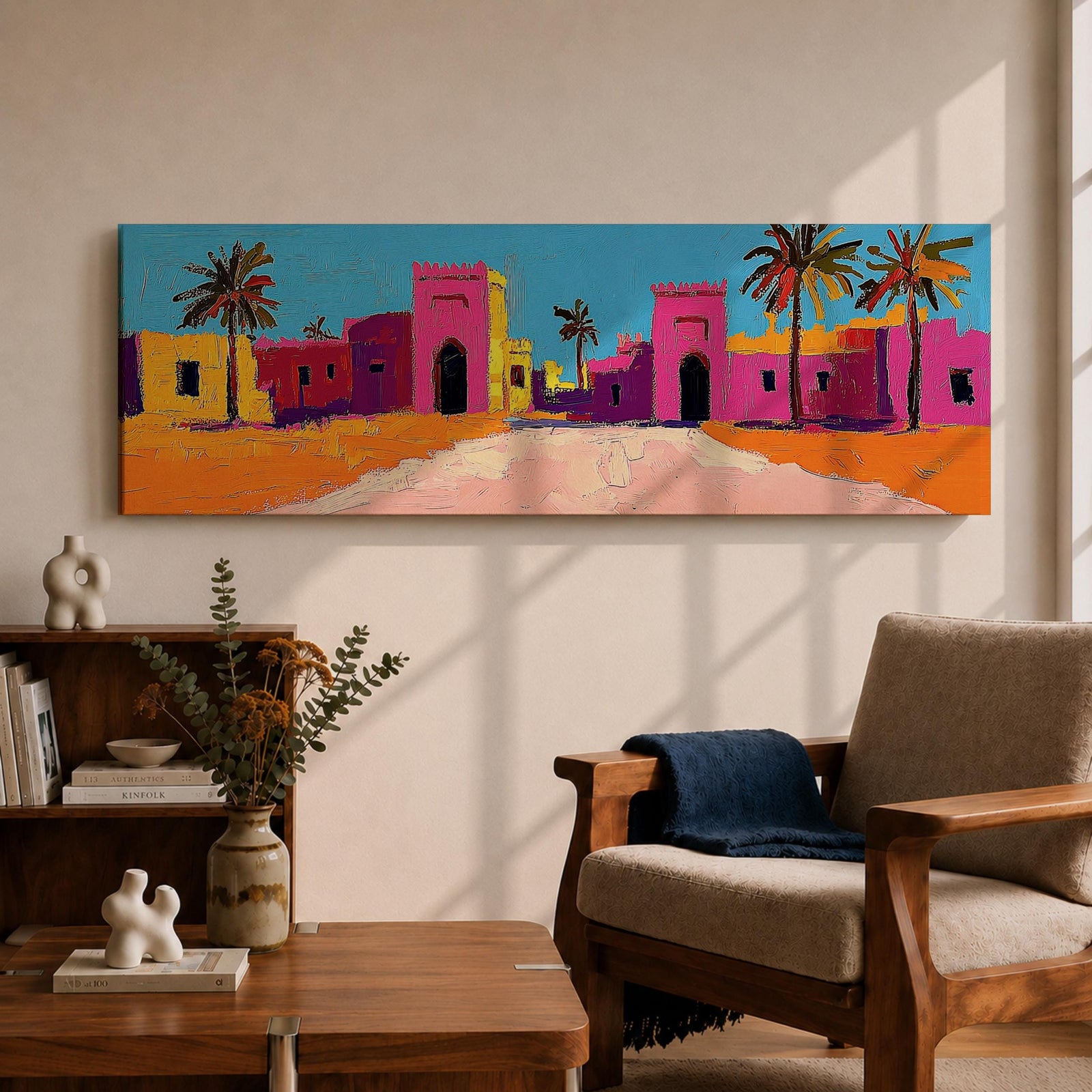 Panoramic desert village painting showing colorful Moroccan kasbah buildings in bright pink and warm ochre tones with tall palm trees lining a sandy road. Bold textured brushstrokes and vibrant colors create a lively North African scene beneath a clear blue sky across the wide horizontal composition.