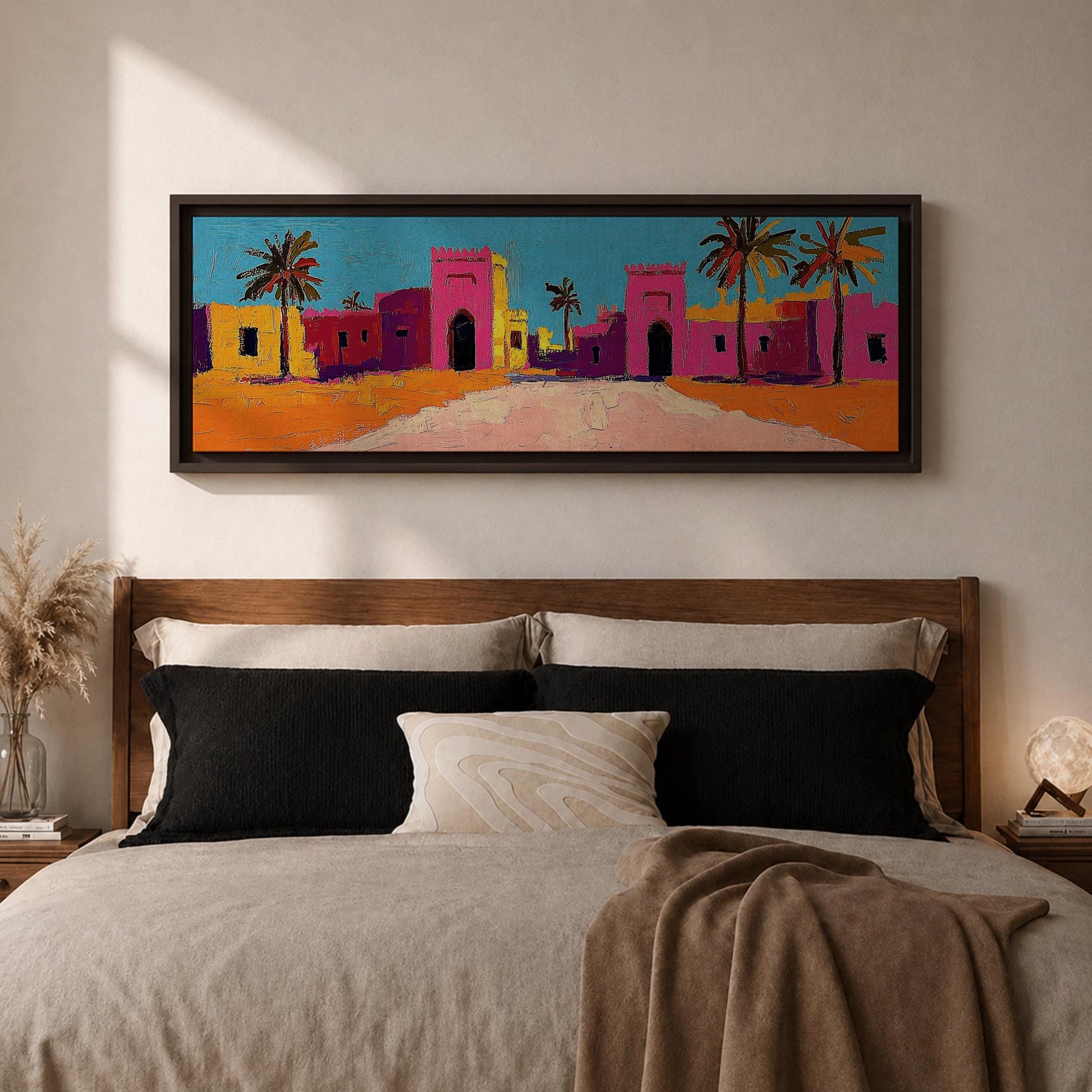 Panoramic desert village painting showing colorful Moroccan kasbah buildings in bright pink and warm ochre tones with tall palm trees lining a sandy road. Bold textured brushstrokes and vibrant colors create a lively North African scene beneath a clear blue sky across the wide horizontal composition.