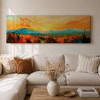 Panoramic desert sunset painting showing distant layered mountains beneath a glowing sun with sweeping orange and gold skies. Thick textured brushstrokes form desert plants and rocky terrain in the foreground while teal and blue ridges fade into the horizon, creating a wide southwestern landscape composition.