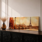A long panoramic watercolor style painting of the Eiffel Tower rising above the Paris skyline beside the Seine River. Warm autumn foliage frames the scene while a bridge crosses the river and historic buildings sit beneath a glowing sky, creating a romantic Paris cityscape in a wide horizontal composition.