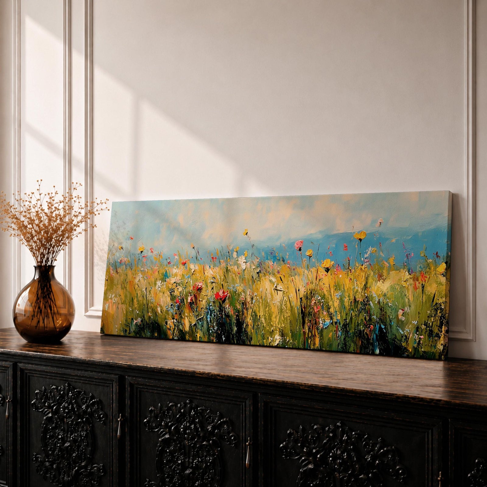 Panoramic wildflower meadow painting featuring tall golden grasses mixed with scattered red, yellow, and blue flowers swaying across an open field. Loose textured brushstrokes create depth through the meadow while a soft blue sky and distant horizon stretch across the wide landscape composition.