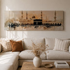 Panoramic painting of the Kaaba at Masjid Al Haram in Mecca surrounded by mosque arches and tall minarets. The sacred black cube stands at the center of a wide courtyard with crowds gathered around while warm golden tones and architectural details stretch across the expansive skyline.