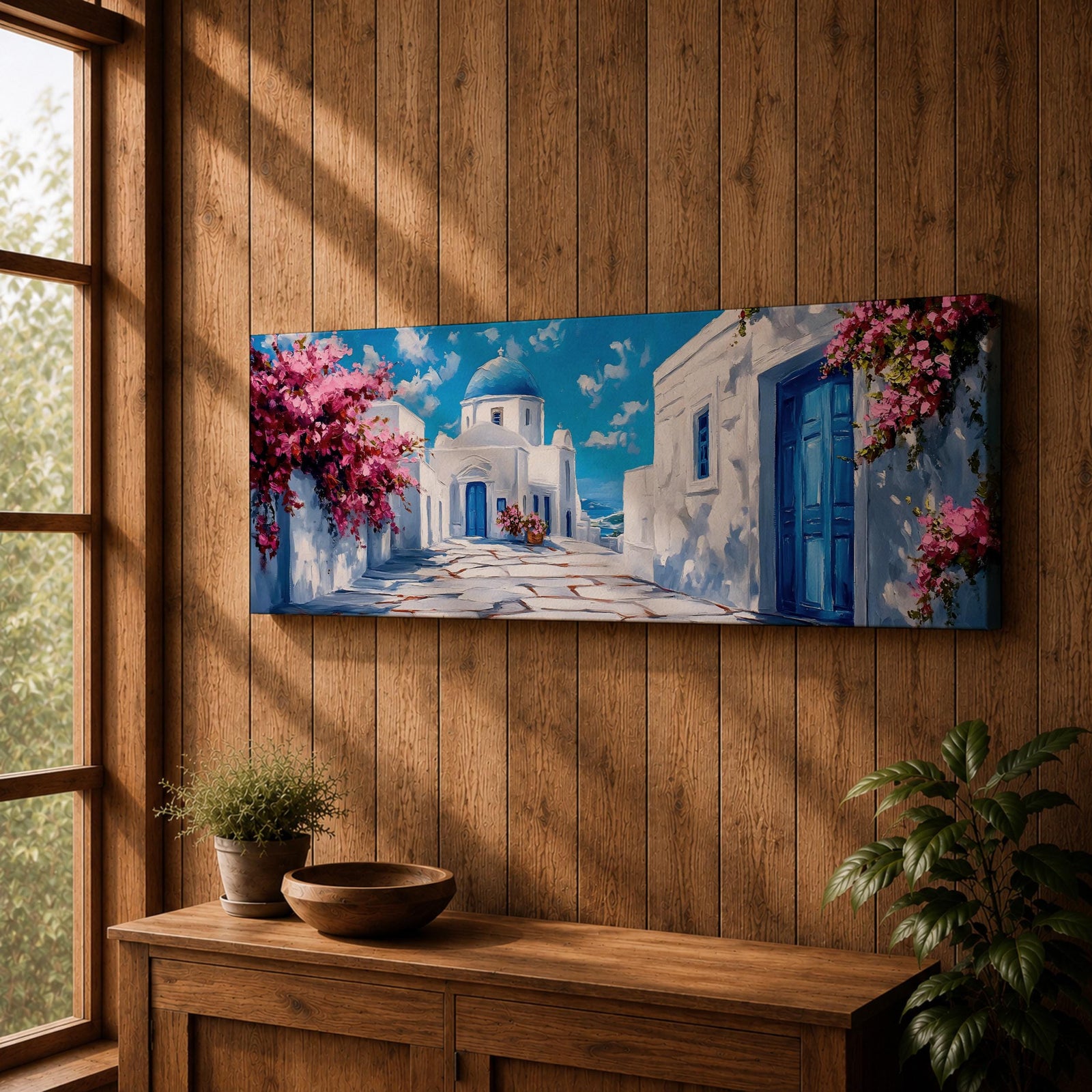 Panoramic painting of a Santorini village featuring whitewashed buildings with blue doors and a domed church along a sunlit stone pathway. Pink bougainvillea flowers frame the scene while bright blue sky and distant Aegean Sea appear beyond the island architecture across the wide composition.