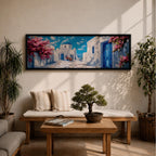 Panoramic painting of a Santorini village featuring whitewashed buildings with blue doors and a domed church along a sunlit stone pathway. Pink bougainvillea flowers frame the scene while bright blue sky and distant Aegean Sea appear beyond the island architecture across the wide composition.
