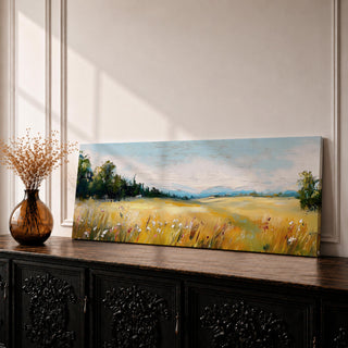 Panoramic countryside landscape painting showing a wide golden field filled with tall grasses and scattered wildflowers. A tree line borders the meadow while distant hills stretch across the horizon beneath a soft blue sky with light clouds across the expansive rural scene.