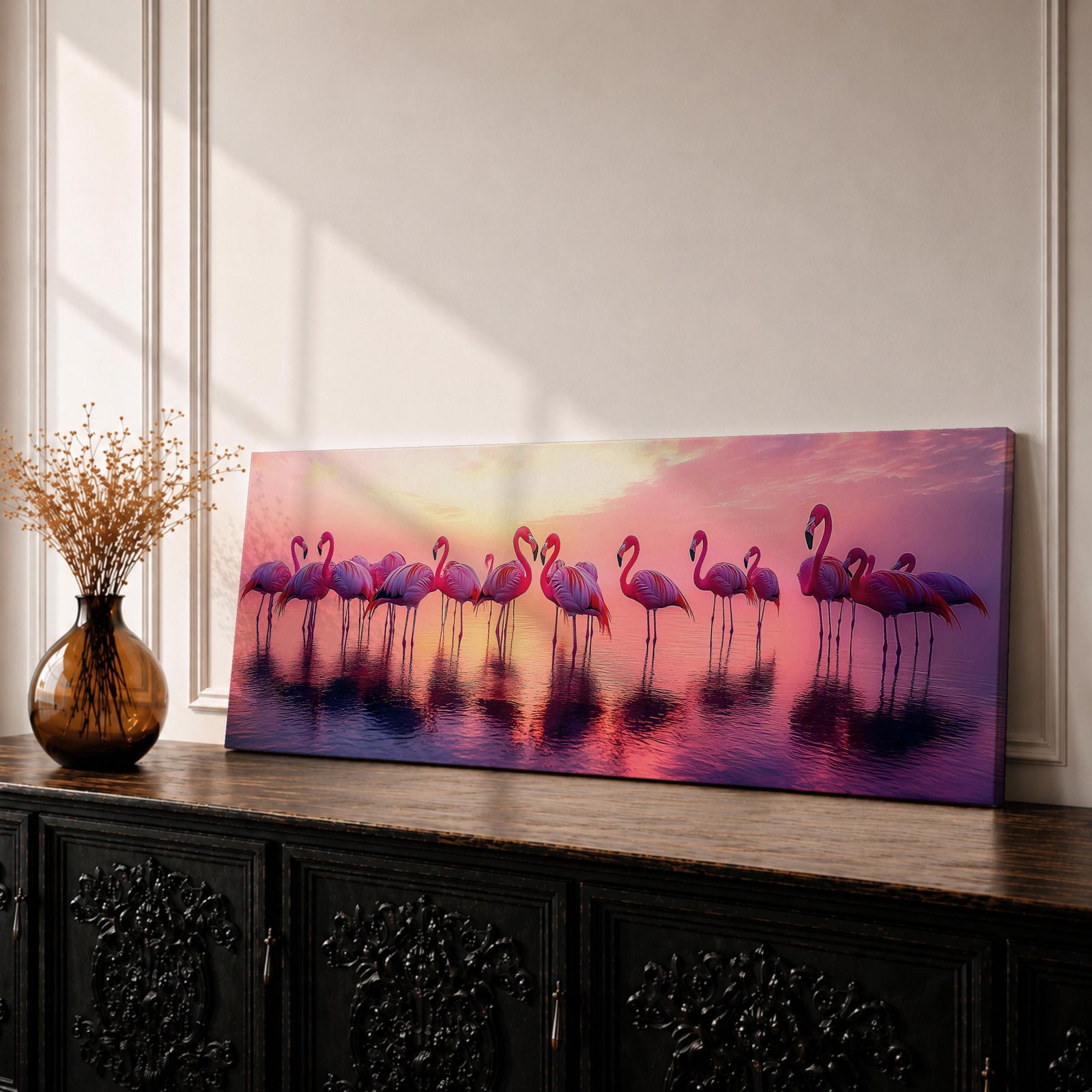 Panoramic artwork showing a flock of flamingos standing in shallow reflective water at sunset. The long horizontal composition features pink birds mirrored in the calm lake surface with glowing orange, purple, and magenta sky tones behind them, creating a tropical waterscape with silhouettes and soft reflections stretching across the scene.