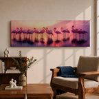 Panoramic artwork showing a flock of flamingos standing in shallow reflective water at sunset. The long horizontal composition features pink birds mirrored in the calm lake surface with glowing orange, purple, and magenta sky tones behind them, creating a tropical waterscape with silhouettes and soft reflections stretching across the scene.