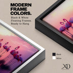 Panoramic artwork showing a flock of flamingos standing in shallow reflective water at sunset. The long horizontal composition features pink birds mirrored in the calm lake surface with glowing orange, purple, and magenta sky tones behind them, creating a tropical waterscape with silhouettes and soft reflections stretching across the scene.