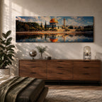 Panoramic canvas artwork depicting the Dome of the Rock in Jerusalem with its iconic golden dome and blue tiled octagonal structure rising above surrounding trees and historic buildings, reflected in calm water in the foreground beneath a bright sky filled with scattered clouds, rendered in a detailed landscape style emphasizing the architecture and skyline of the sacred site.