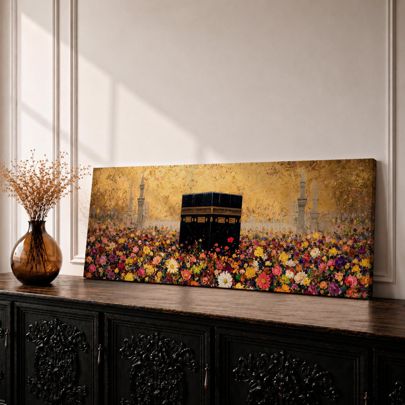 A panoramic painting of the Kaaba standing at the center of a vibrant field of colorful flowers with red, pink, yellow, and white blossoms stretching across the foreground, set against a glowing gold textured background with faint mosque silhouettes and minarets surrounding the sacred structure.