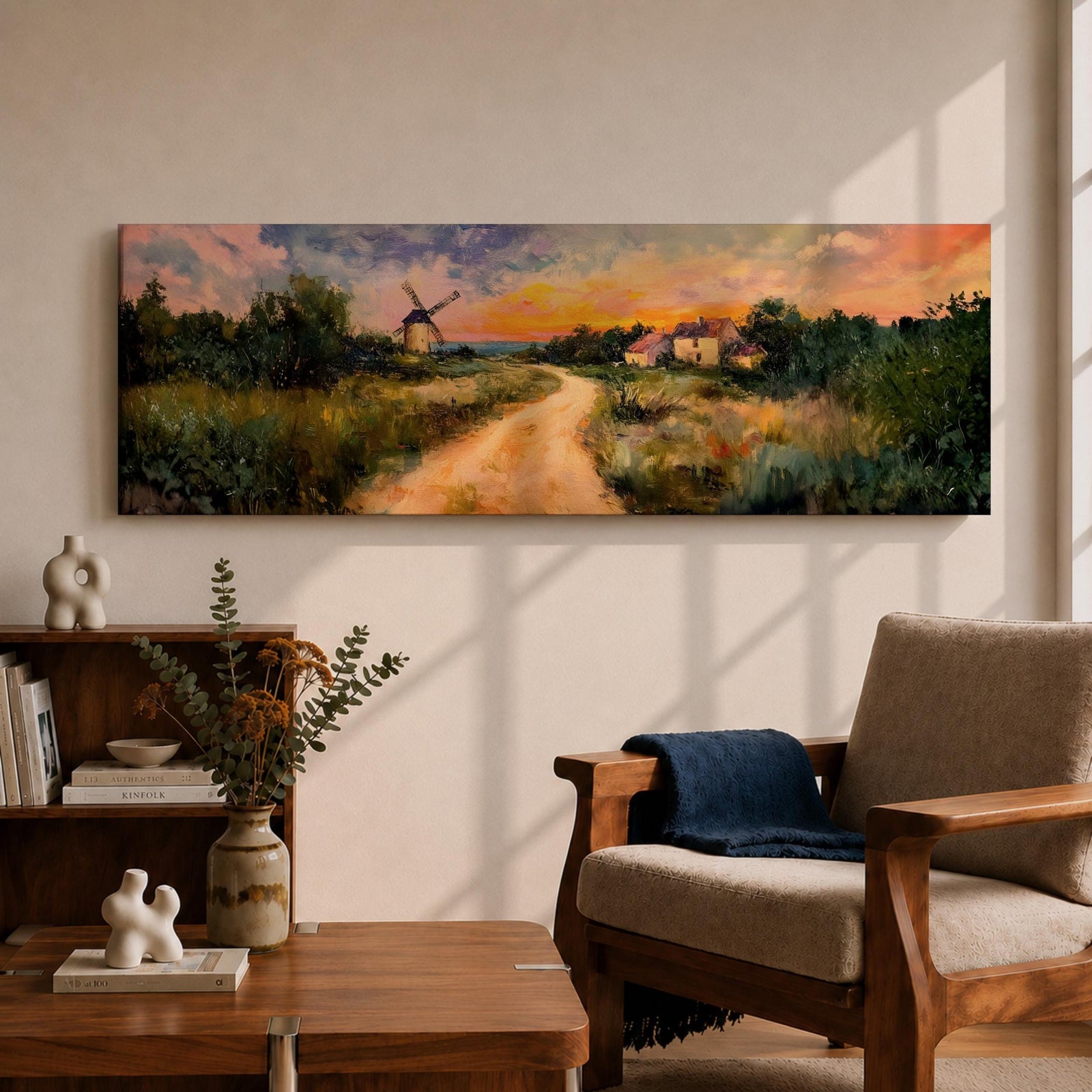 A panoramic countryside landscape painting showing a winding dirt road leading through grassy fields toward a traditional windmill and small farmhouse under a glowing sunset sky, with soft clouds and warm golden light illuminating the rural scenery across the wide composition.
