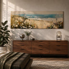 A long panoramic coastal painting showing sandy dunes covered with wild grasses and small white flowers overlooking a calm ocean shoreline. Soft waves roll toward the beach beneath a pale blue sky while textured brush strokes create a peaceful seascape landscape stretching across a wide horizontal composition.