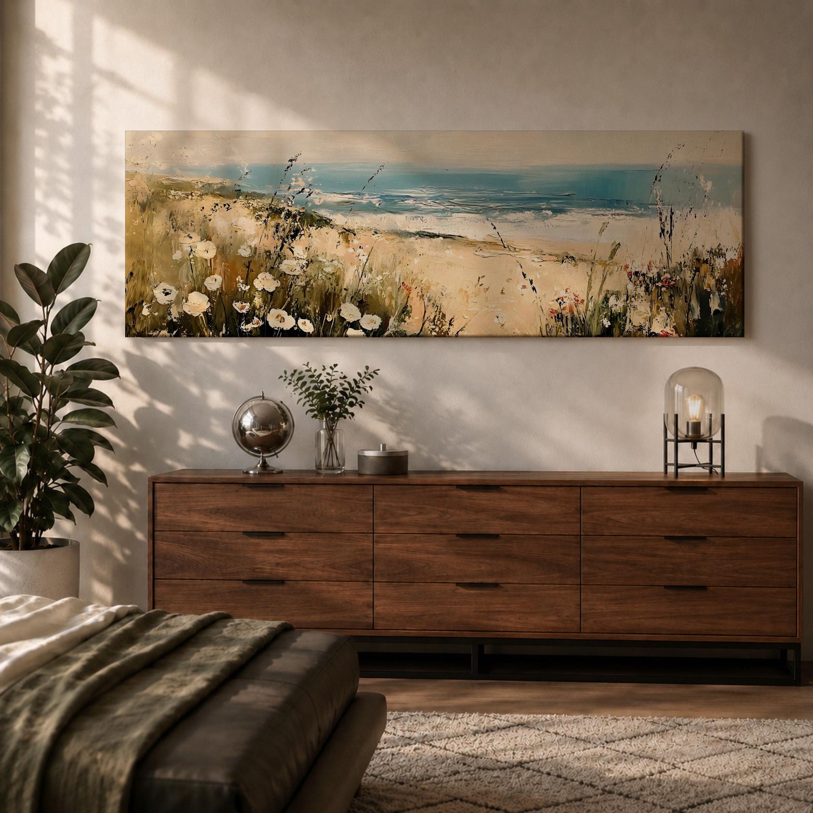 A long panoramic coastal painting showing sandy dunes covered with wild grasses and small white flowers overlooking a calm ocean shoreline. Soft waves roll toward the beach beneath a pale blue sky while textured brush strokes create a peaceful seascape landscape stretching across a wide horizontal composition.