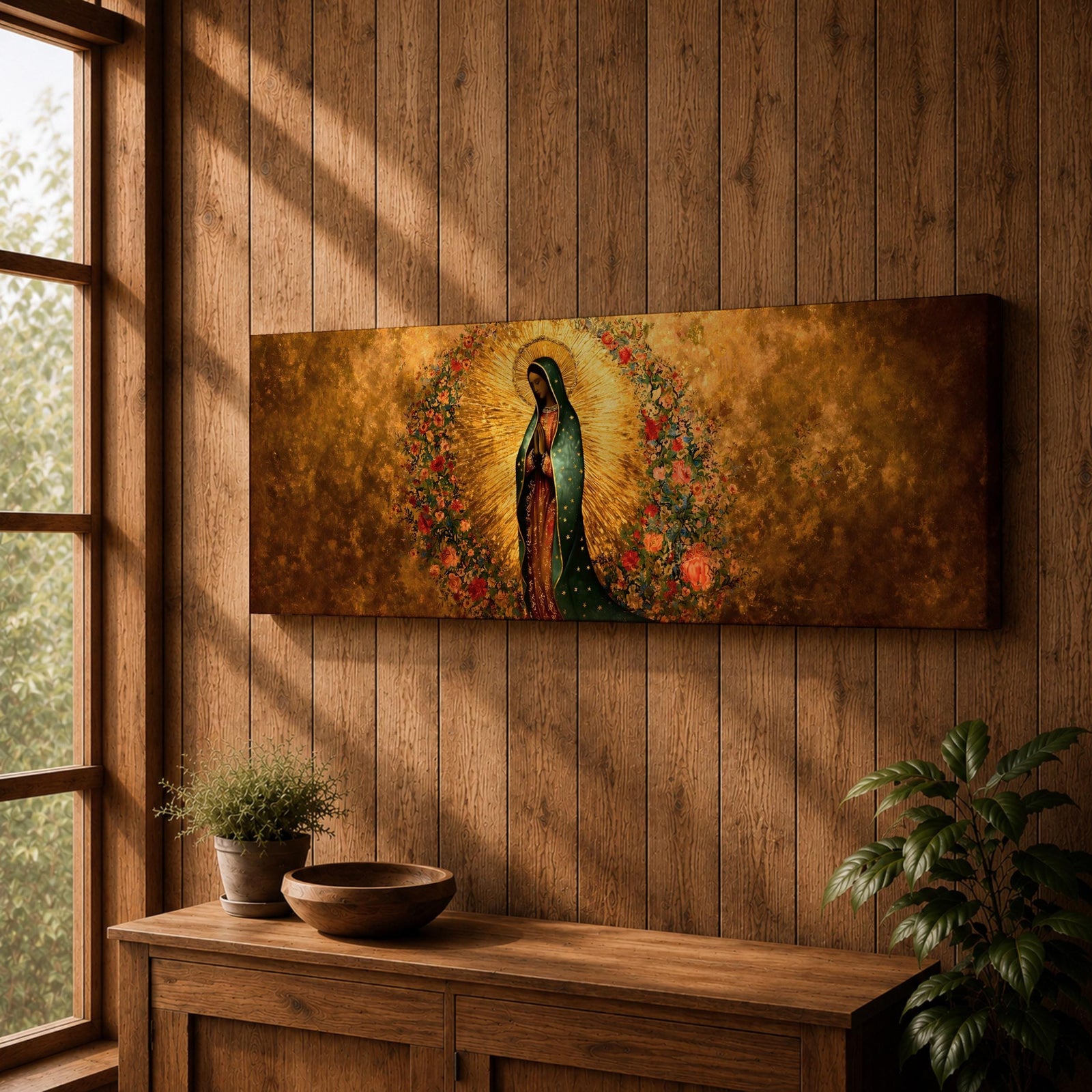 A long panoramic artwork depicting Our Lady of Guadalupe standing in prayer with folded hands and bowed head. She wears a green star covered mantle over a rose colored gown and is surrounded by radiant golden rays and a wreath of vibrant flowers, forming a traditional Catholic Marian image in a wide horizontal composition.