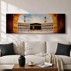 A long panoramic artwork depicting the Kaaba at the center of Masjid Al Haram in Mecca framed by grand mosque arches and tall minarets. The sacred black cube stands in the courtyard while pilgrims gather around it, creating a wide horizontal composition highlighting the holy Islamic sanctuary.