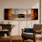 A long panoramic artwork depicting the Kaaba at the center of Masjid Al Haram in Mecca framed by grand mosque arches and tall minarets. The sacred black cube stands in the courtyard while pilgrims gather around it, creating a wide horizontal composition highlighting the holy Islamic sanctuary.