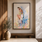 A watercolor style framed canvas depicting Virgin Mary in profile, wearing a blue and white veil with gold trim, holding a rosary and praying, surrounded by soft floral colors and a gentle light background.