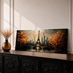 A long narrow panoramic painting depicts the Eiffel Tower rising above a river with an arched bridge in the foreground, surrounded by autumn trees and a distant city skyline, rendered in textured brushstrokes with warm golden tones and soft reflections that create depth and a romantic atmospheric cityscape.