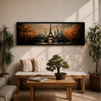 A long narrow panoramic painting depicts the Eiffel Tower rising above a river with an arched bridge in the foreground, surrounded by autumn trees and a distant city skyline, rendered in textured brushstrokes with warm golden tones and soft reflections that create depth and a romantic atmospheric cityscape.