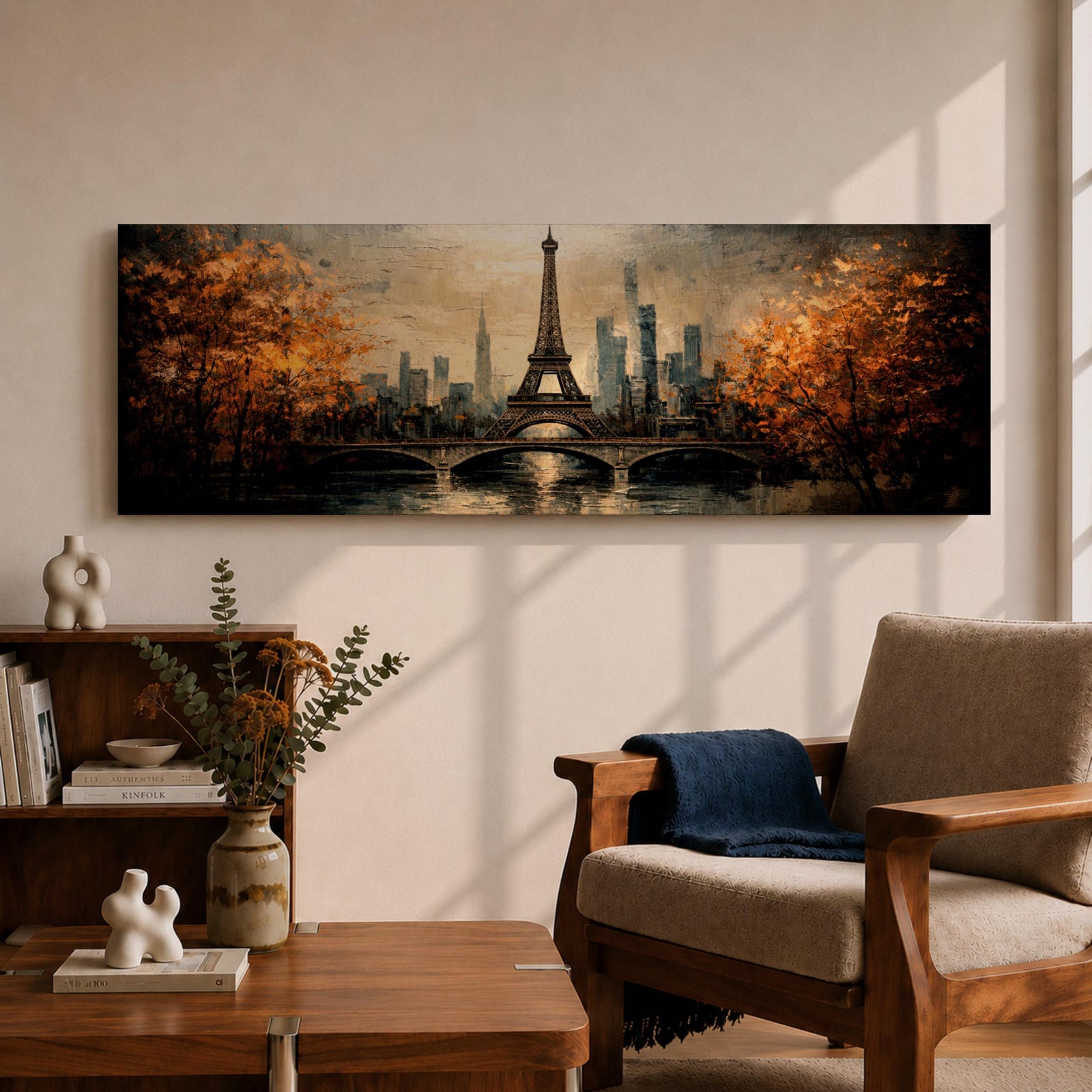 A long narrow panoramic painting depicts the Eiffel Tower rising above a river with an arched bridge in the foreground, surrounded by autumn trees and a distant city skyline, rendered in textured brushstrokes with warm golden tones and soft reflections that create depth and a romantic atmospheric cityscape.