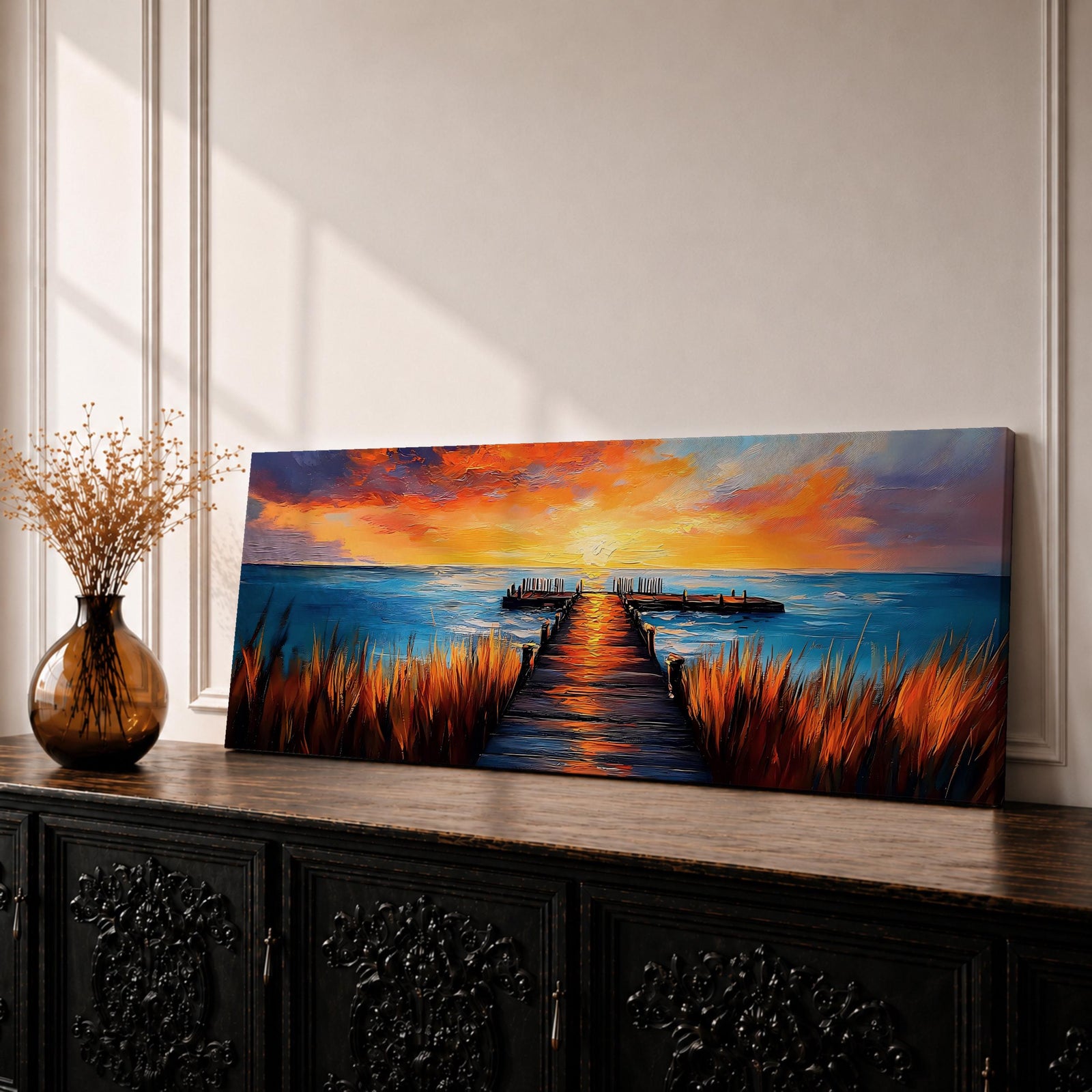 A long narrow panoramic painting depicts a wooden pier extending through tall grasses into calm ocean waters, leading toward a glowing sunset on the horizon, with bold textured brushstrokes and vivid color contrasts capturing reflections of warm light across the water and sky in an expressive contemporary style.
